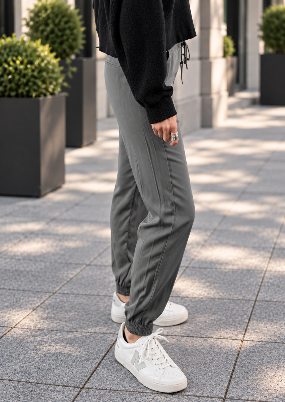A person wearing gray jogger-style pants with elastic cuffs, paired with a black long-sleeve top and white sneakers, standing on a paved outdoor walkway.